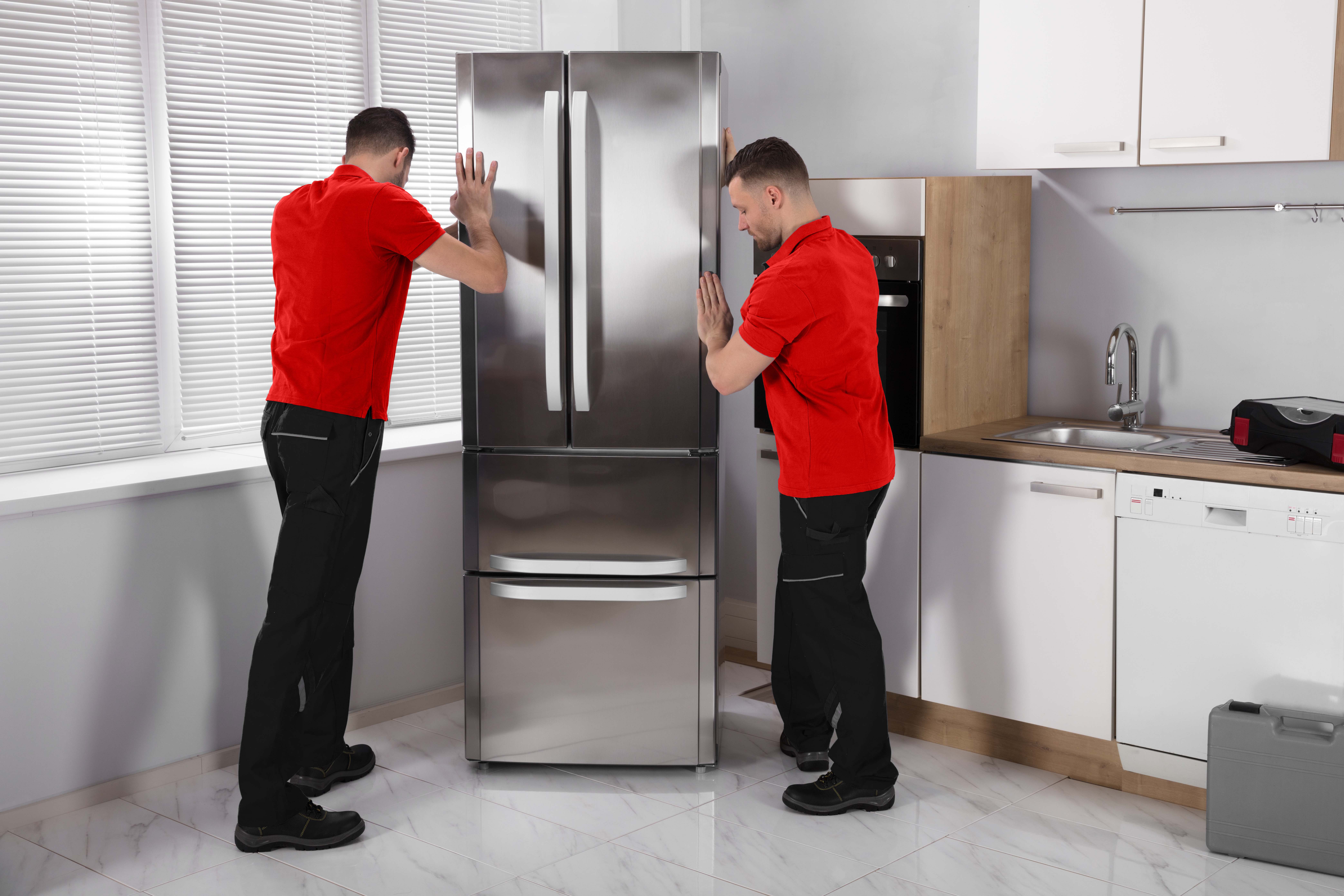 Two movers positioning refrigerator in kitchen during commercial move