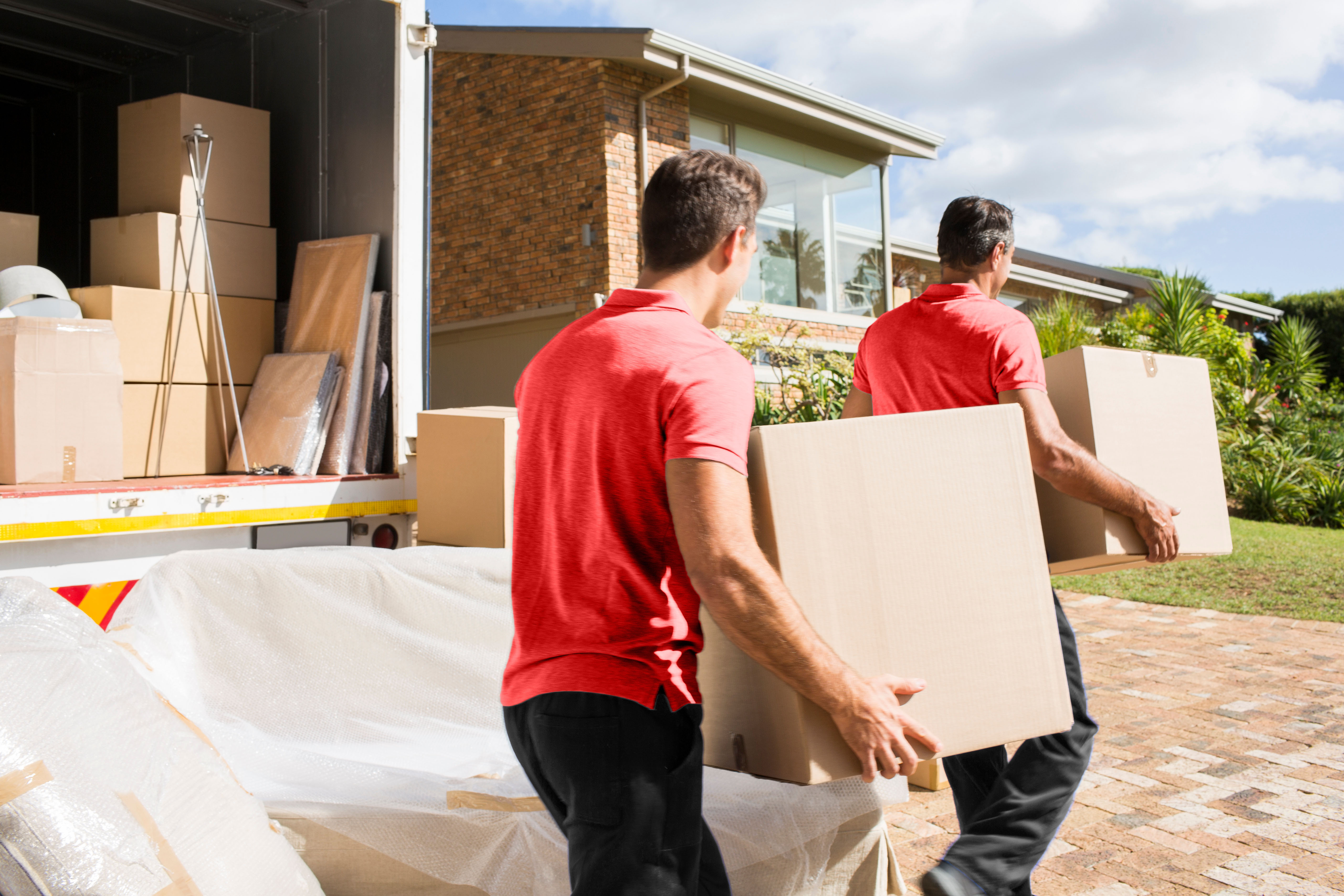 Two Desert Moving movers carrying boxes from truck to suburban home